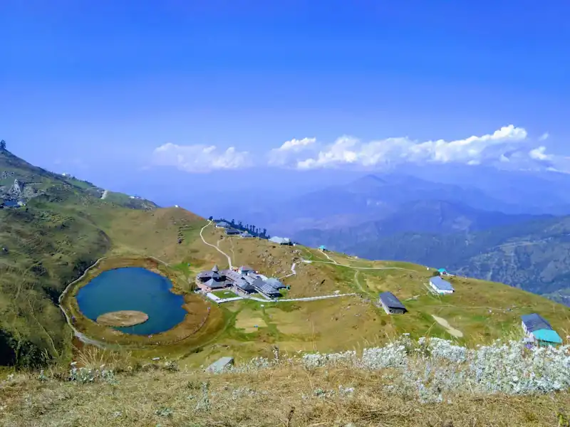 A tented camp in a green meadow below rocky ridges.